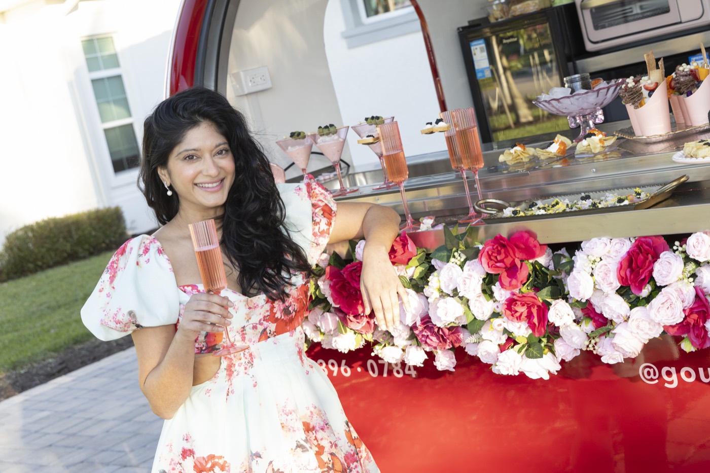 Nisha leaning on the Chariot's flower ledge with a glass of rosé