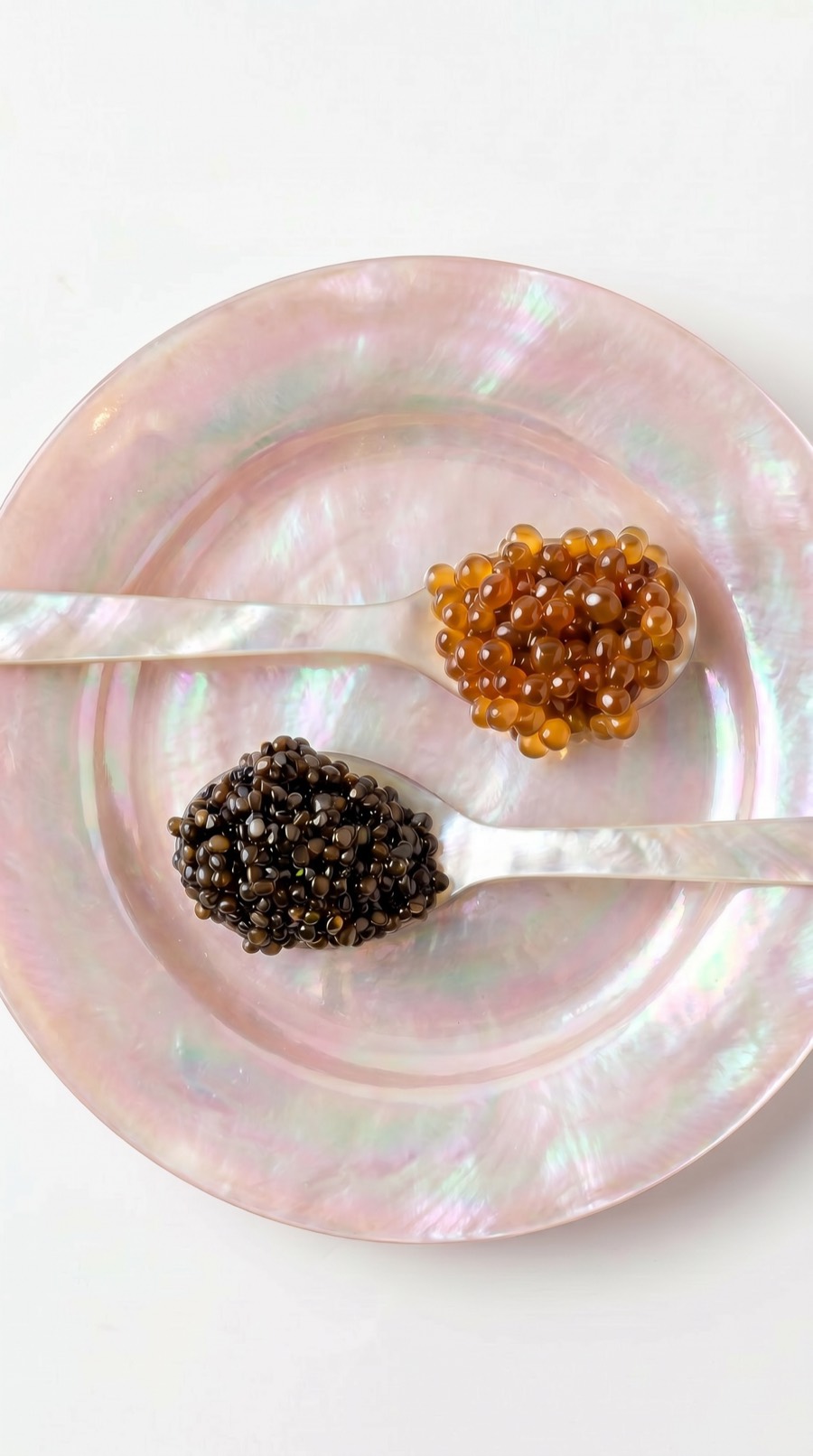 Two mother-of-pearl spoons of caviar on a blush pearl plate