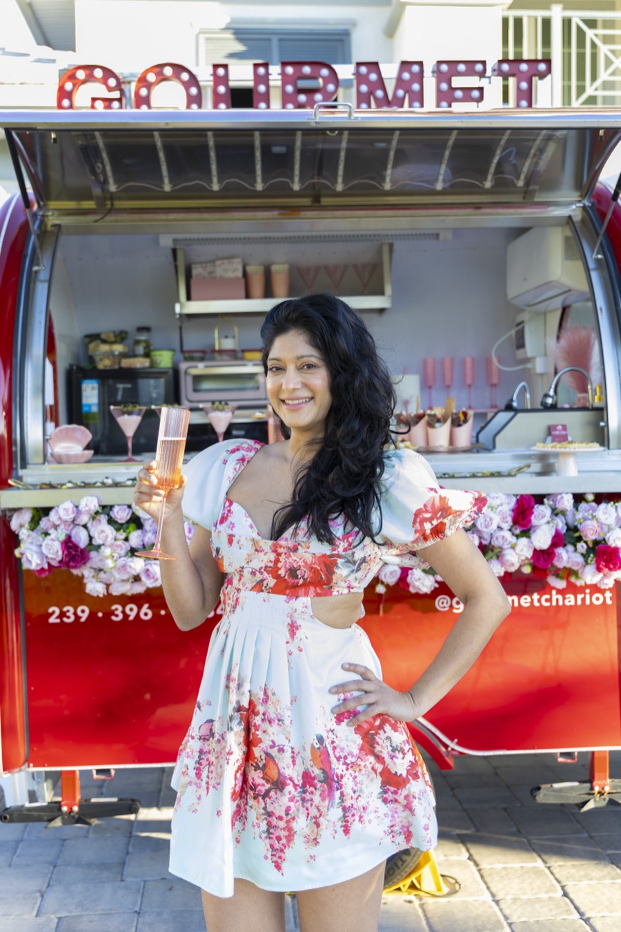 Nisha Singh, founder of Gourmet Chariot, standing in front of the Chariot with a glass of champagne