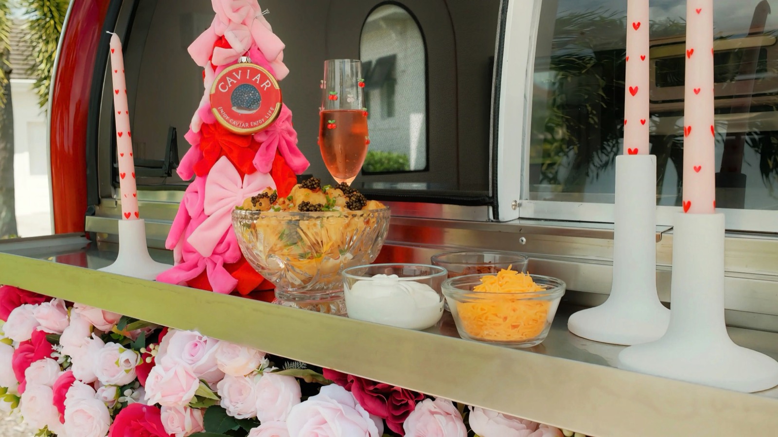 The Chariot ledge dressed for the holidays: a pink bow tree with a caviar ornament, a crystal bowl of caviar-topped bites, heart-print candles and a glass of rosé above the roses